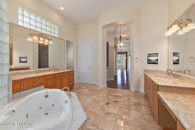 full bathroom featuring a tub with jets, baseboards, a towering ceiling, and a sink