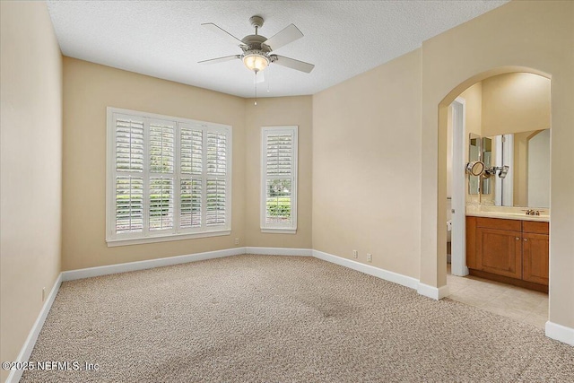 spare room with light carpet, arched walkways, a textured ceiling, and ceiling fan