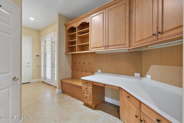 unfurnished office featuring light tile patterned floors, built in desk, and baseboards