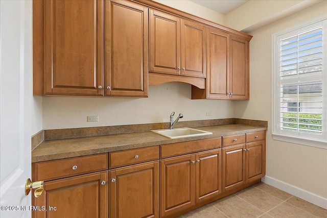 kitchen with light tile patterned floors, baseboards, a sink, dark countertops, and brown cabinets