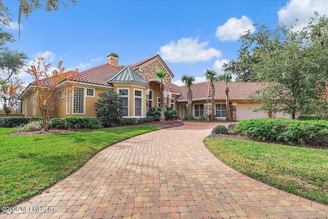 mediterranean / spanish home with a chimney, stucco siding, a front lawn, stone siding, and decorative driveway