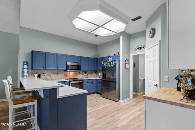 kitchen featuring a kitchen bar, blue cabinets, kitchen peninsula, stainless steel appliances, and decorative backsplash