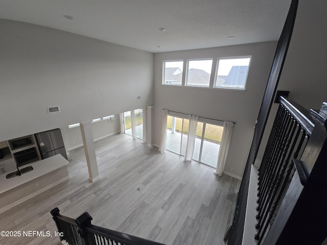 staircase featuring visible vents, baseboards, a high ceiling, and wood finished floors