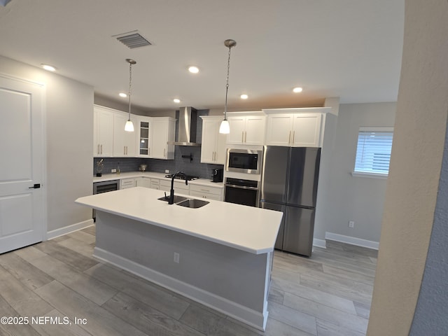 kitchen featuring wall chimney exhaust hood, sink, white cabinetry, appliances with stainless steel finishes, and a kitchen island with sink