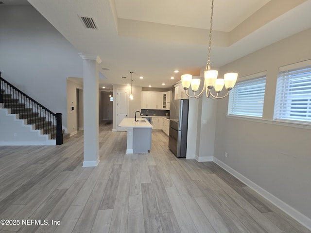 kitchen featuring pendant lighting, stainless steel refrigerator, white cabinetry, an island with sink, and light wood-type flooring