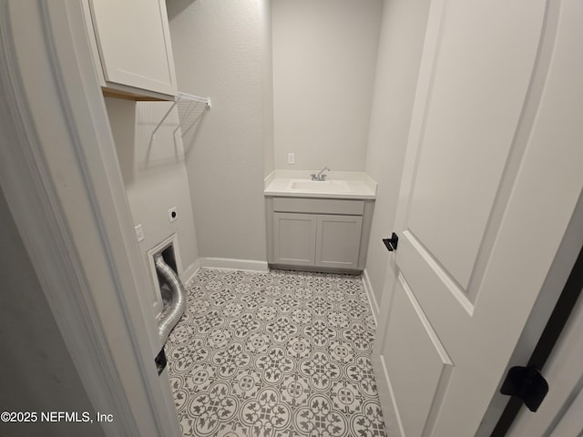 washroom featuring electric dryer hookup, a sink, cabinet space, light tile patterned floors, and baseboards