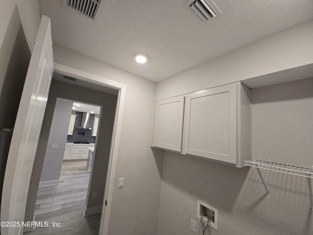 laundry area featuring cabinets, washer hookup, light hardwood / wood-style floors, and a textured ceiling