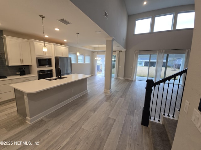 kitchen with visible vents, a center island with sink, a sink, stainless steel appliances, and light wood-style floors