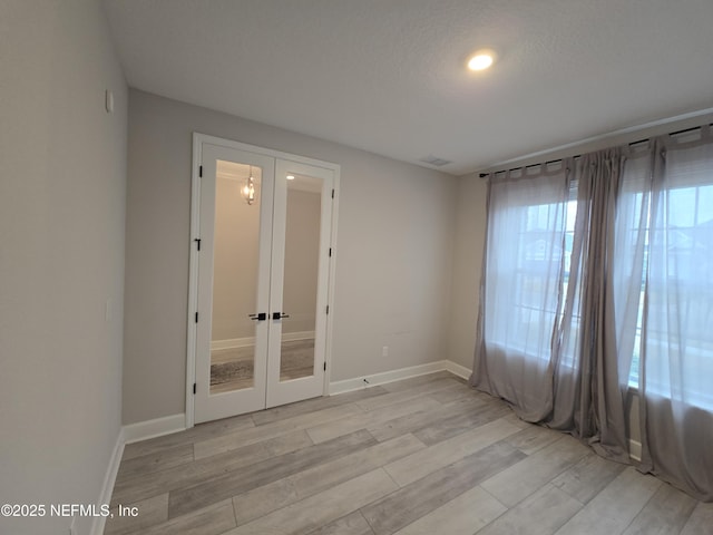 empty room featuring french doors, baseboards, and light wood finished floors