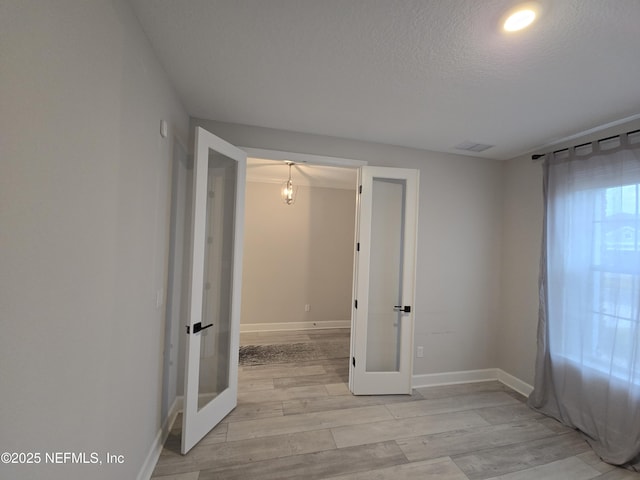 spare room with light hardwood / wood-style floors, french doors, and a textured ceiling