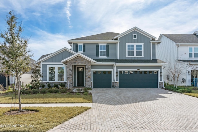 craftsman house featuring board and batten siding, a shingled roof, decorative driveway, stone siding, and an attached garage