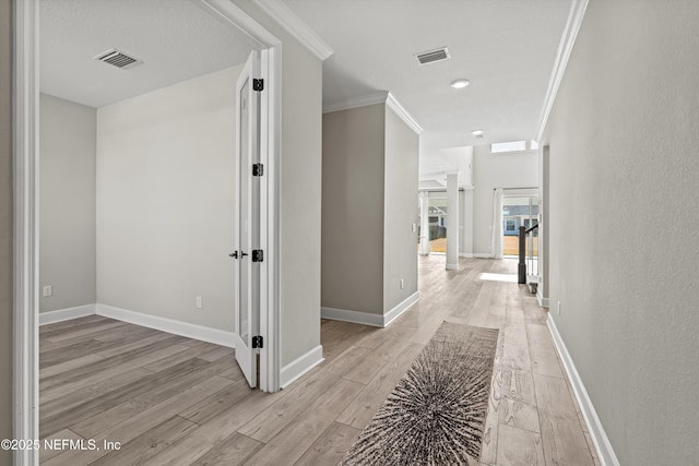 hall with baseboards, light wood-style floors, visible vents, and ornamental molding