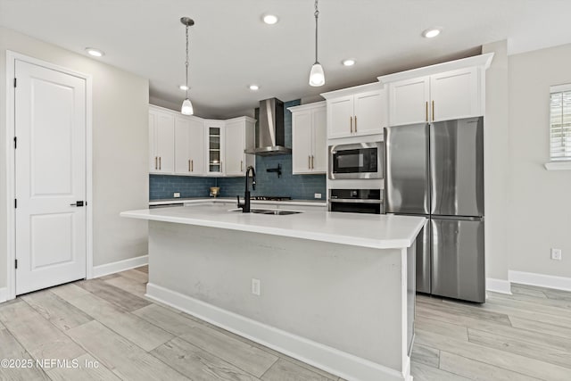 kitchen featuring appliances with stainless steel finishes, a kitchen island with sink, hanging light fixtures, and wall chimney range hood