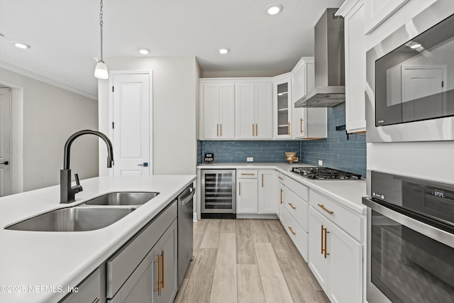 kitchen featuring appliances with stainless steel finishes, white cabinetry, sink, beverage cooler, and wall chimney exhaust hood