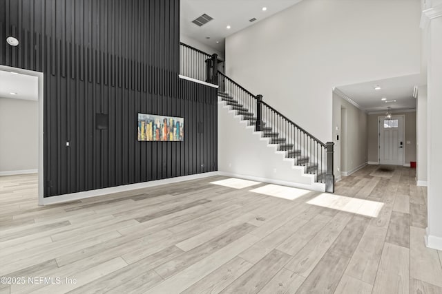 unfurnished living room featuring crown molding, a towering ceiling, and light hardwood / wood-style flooring