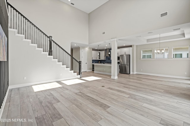 unfurnished living room with a notable chandelier, a tray ceiling, a towering ceiling, and light wood-type flooring