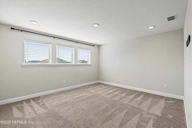 carpeted empty room featuring baseboards, visible vents, and a textured ceiling