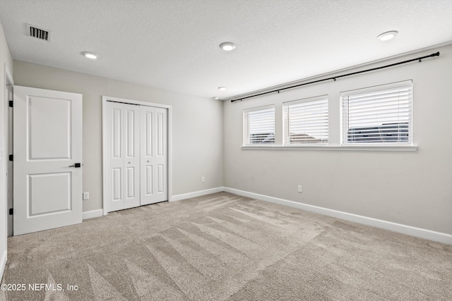 unfurnished bedroom with light colored carpet, a closet, and a textured ceiling