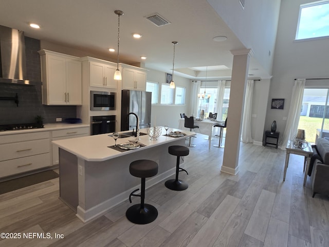 kitchen featuring black appliances, light wood-style flooring, a sink, a breakfast bar area, and wall chimney exhaust hood