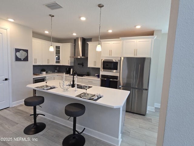 kitchen featuring visible vents, appliances with stainless steel finishes, a kitchen bar, wall chimney range hood, and backsplash