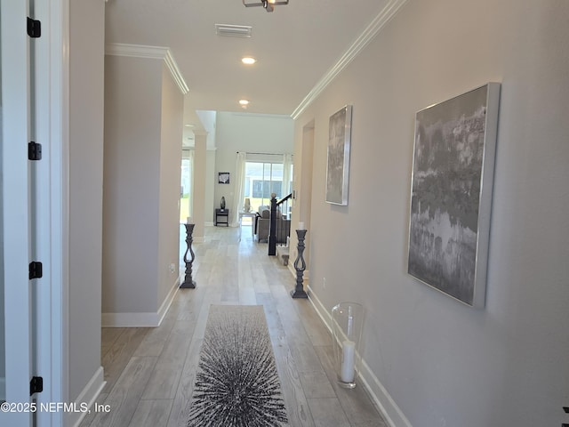 corridor with crown molding, light wood-style floors, visible vents, and baseboards