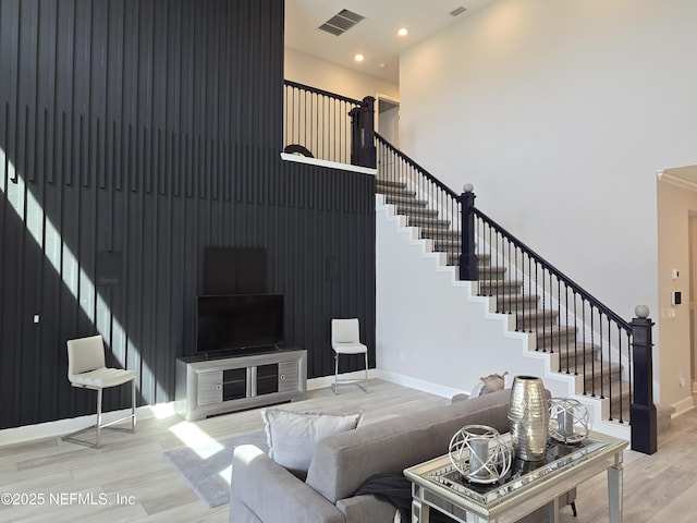 living room featuring visible vents, baseboards, stairs, a towering ceiling, and wood finished floors