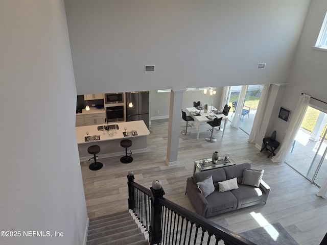 staircase with visible vents, wood finished floors, a towering ceiling, and ornate columns