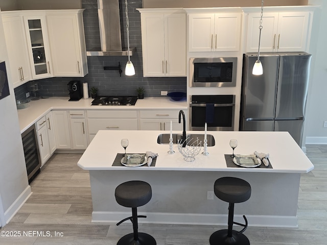 kitchen with a sink, wall chimney exhaust hood, a kitchen bar, and stainless steel appliances