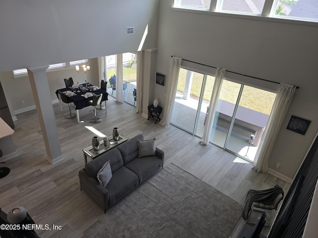 living room featuring a high ceiling, wood finished floors, baseboards, visible vents, and ornate columns