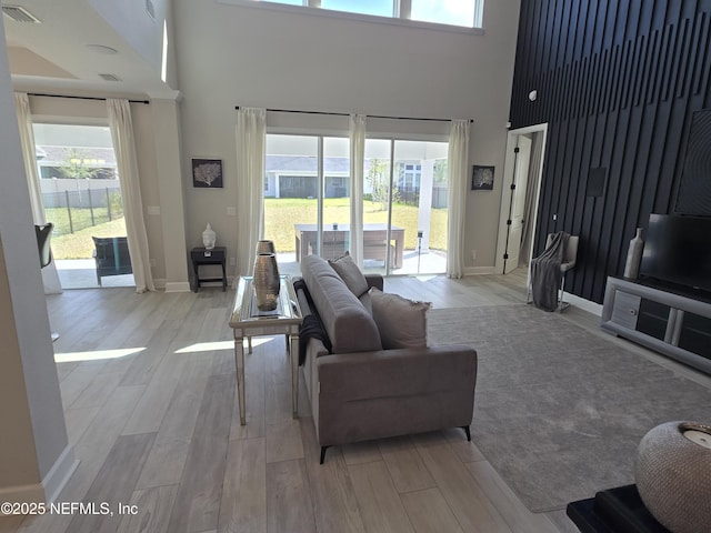 living room featuring baseboards, light wood-type flooring, visible vents, and a towering ceiling