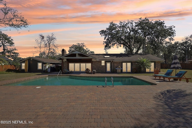 pool at dusk featuring a patio and an outdoor structure