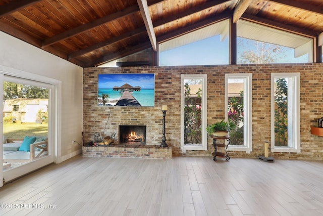 unfurnished living room with light hardwood / wood-style flooring, high vaulted ceiling, a fireplace, brick wall, and beamed ceiling