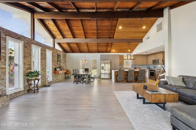 unfurnished living room featuring light hardwood / wood-style flooring, beam ceiling, high vaulted ceiling, brick wall, and wooden ceiling