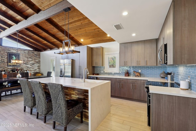 kitchen with wood ceiling, stainless steel appliances, a center island with sink, and light hardwood / wood-style flooring