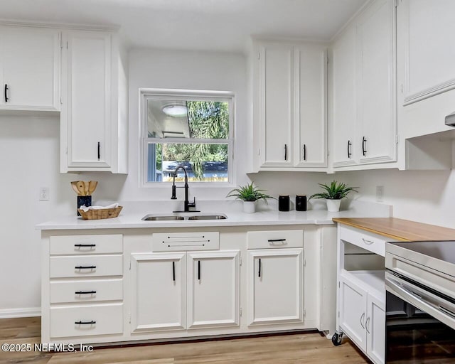 kitchen with white cabinetry, sink, stove, and light wood-type flooring