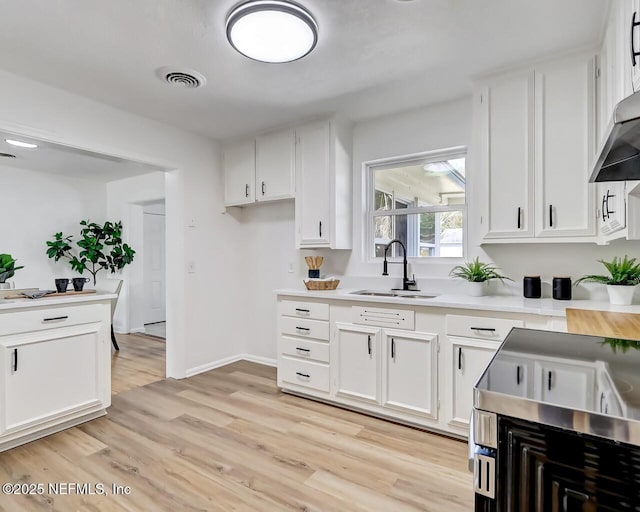 kitchen with extractor fan, sink, white cabinets, and light hardwood / wood-style flooring