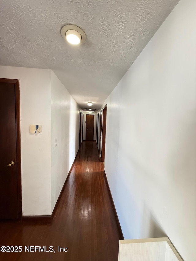 hall featuring dark wood-type flooring and a textured ceiling