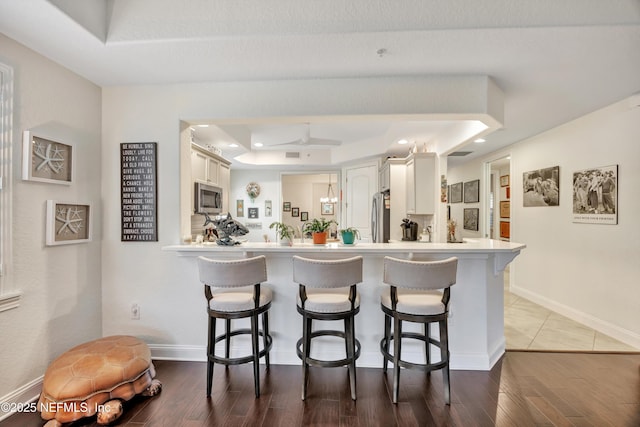 kitchen featuring stainless steel appliances, a kitchen breakfast bar, a tray ceiling, white cabinets, and kitchen peninsula