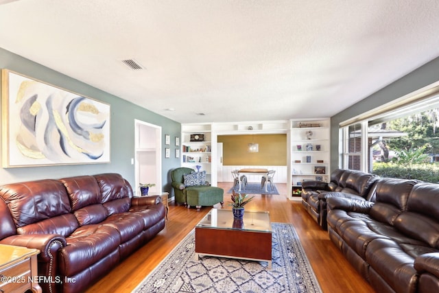 living area featuring built in shelves, wood finished floors, visible vents, and a textured ceiling