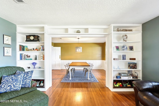 interior space featuring a wainscoted wall, built in shelves, a textured ceiling, and wood finished floors