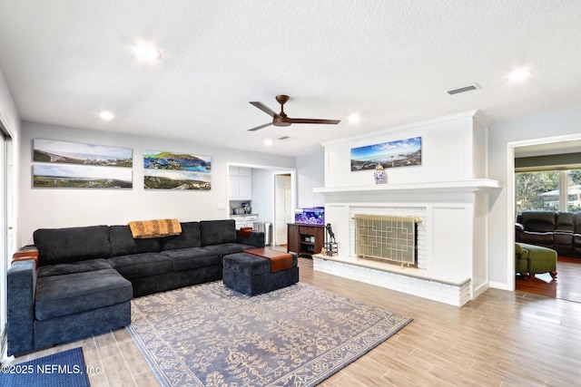 living room featuring visible vents, a brick fireplace, ceiling fan, light wood-style floors, and a textured ceiling