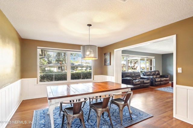 dining space featuring a wainscoted wall, a textured ceiling, and wood finished floors