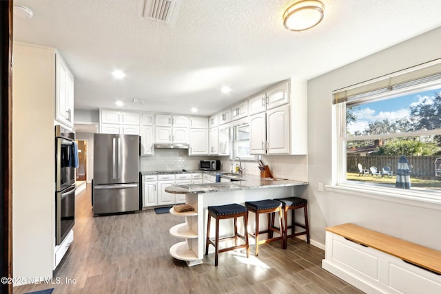 kitchen featuring wood finished floors, white cabinetry, appliances with stainless steel finishes, a peninsula, and decorative backsplash