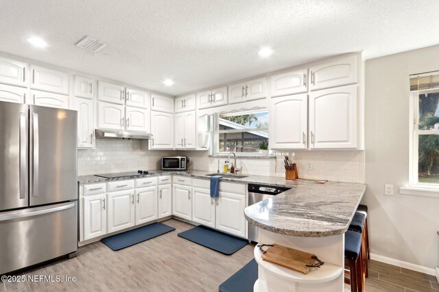 kitchen with under cabinet range hood, light wood-style floors, white cabinets, stainless steel appliances, and a sink