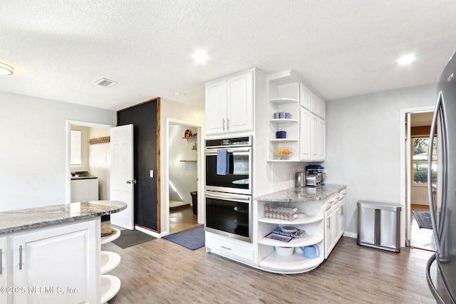 kitchen featuring visible vents, open shelves, light stone counters, stainless steel appliances, and white cabinets