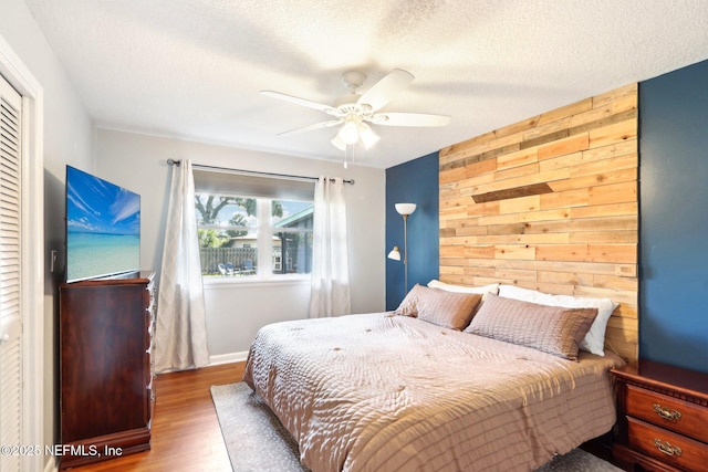 bedroom with a textured ceiling, wood finished floors, wood walls, ceiling fan, and an accent wall