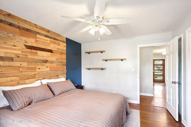 bedroom with wooden walls, baseboards, a textured ceiling, a ceiling fan, and dark wood-style flooring