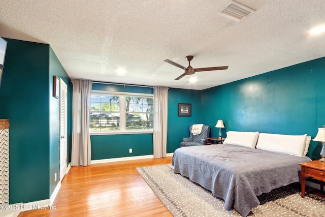 bedroom with a ceiling fan, baseboards, visible vents, light wood finished floors, and a textured ceiling