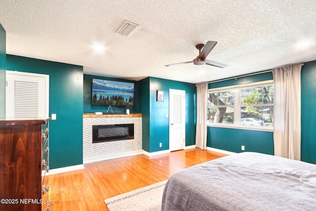 bedroom featuring visible vents, a ceiling fan, wood finished floors, a fireplace, and baseboards