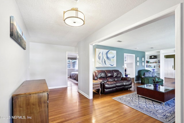 living room with built in shelves, a textured ceiling, baseboards, and wood finished floors